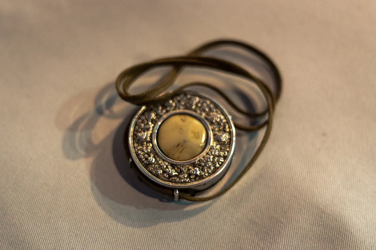 The round silver reliquary Lama Ole Nydahl blessed with, embossed and set with a pale stone, resting on cloth with its braided cord