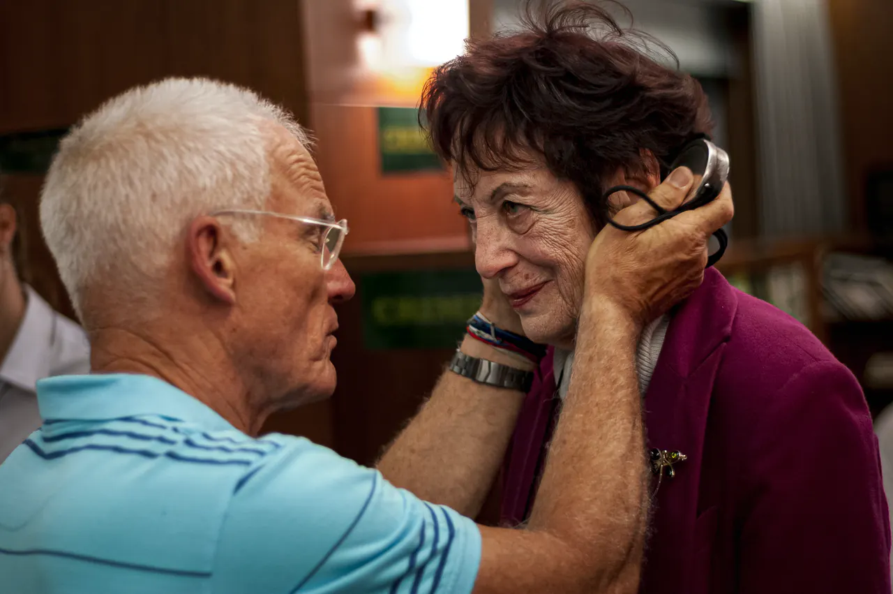 Lama Ole Nydahl in a pale blue polo shirt cups the head of a smiling older woman