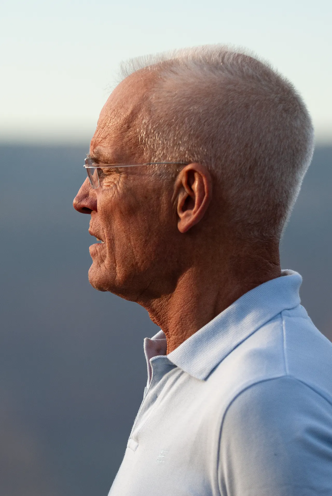 Profile of Lama Ole Nydahl in a pale blue polo shirt against distant desert hills