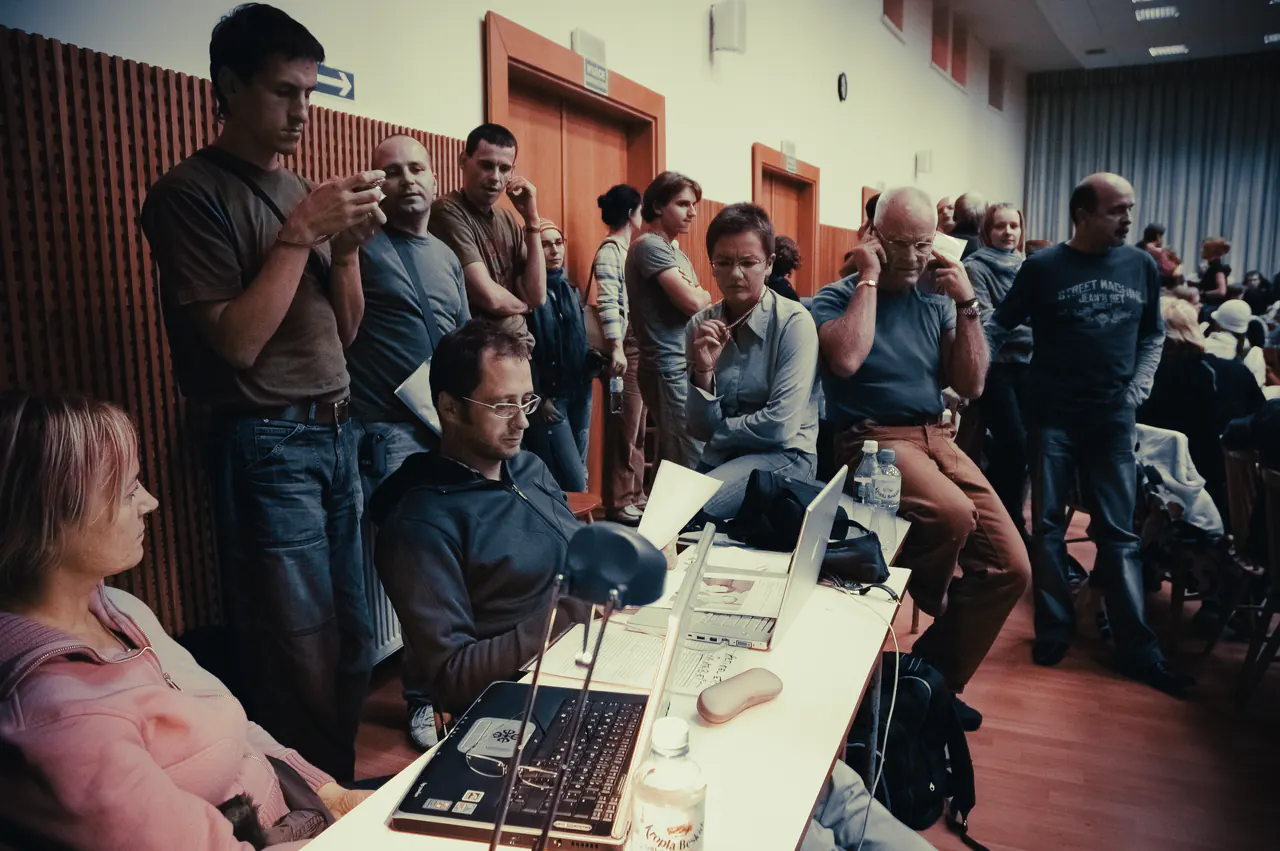 Helpers and visitors gathered around a table of laptops and papers at the back of a lecture hall