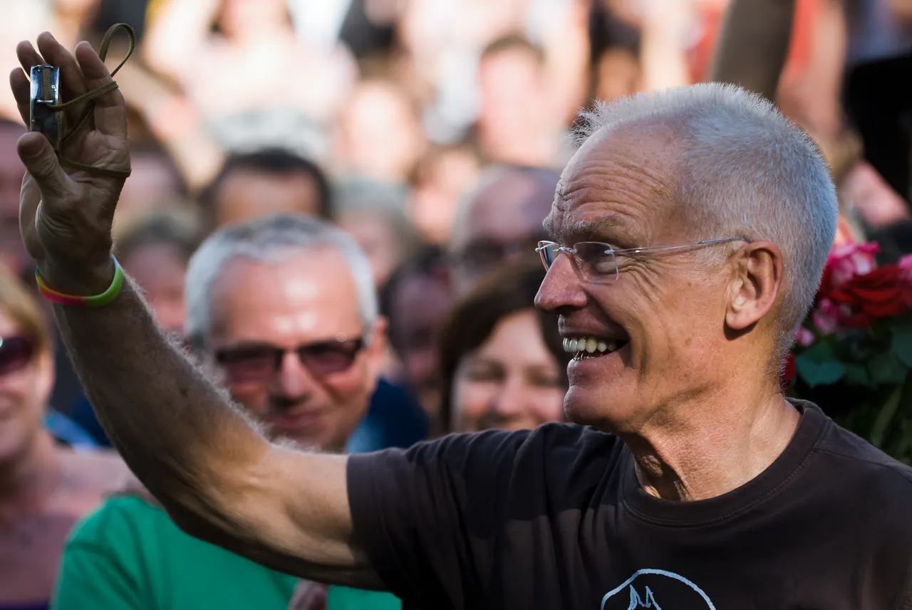Lama Ole Nydahl raises his hand to a smiling crowd outdoors