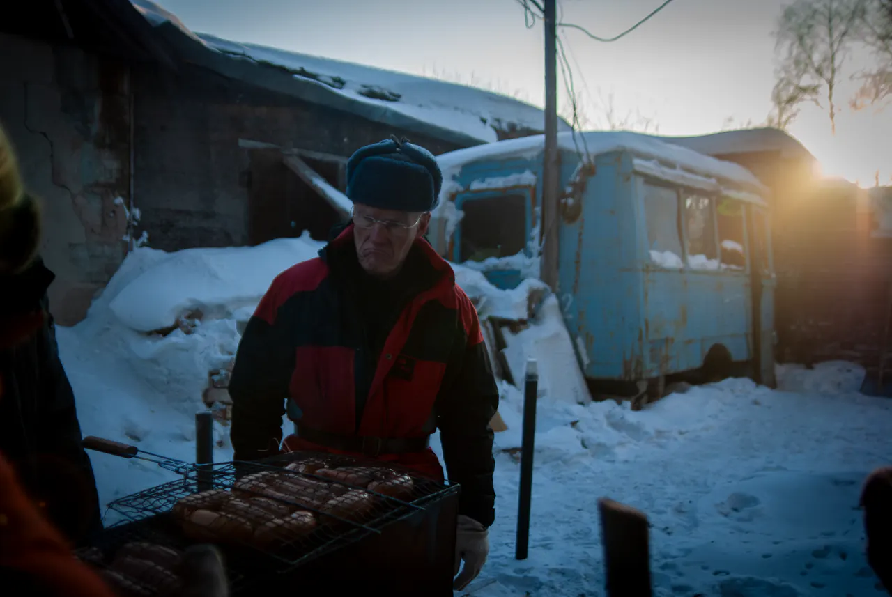 Sausages grill over an open fire in the snow beside an old bus
