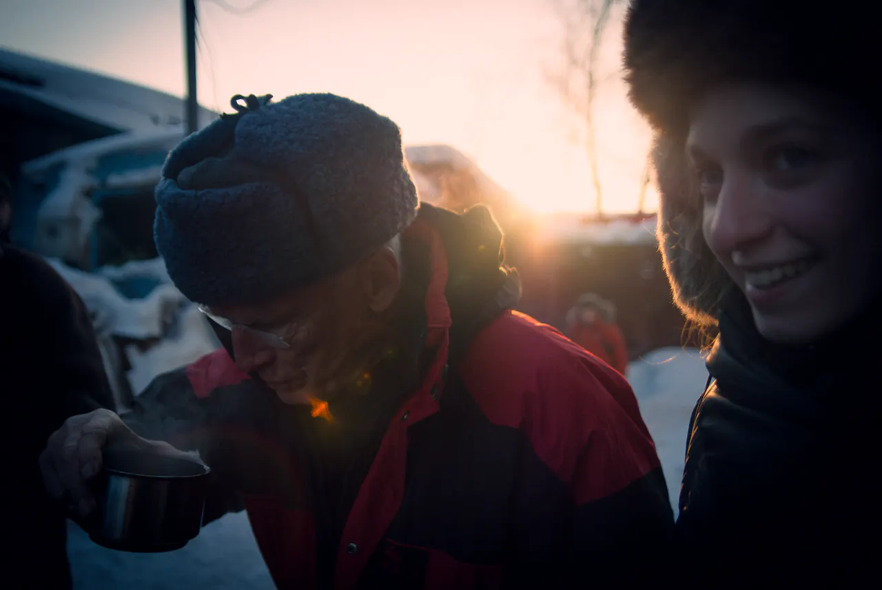 At sunrise in the snow, Lama Ole Nydahl drinks from a thermos cup beside a smiling young woman