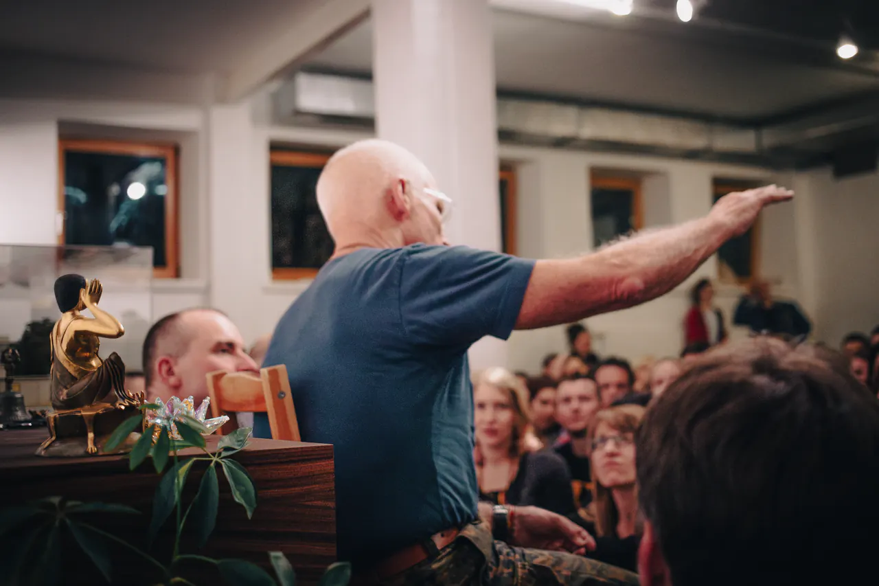 Lama Ole Nydahl stretches out his arm while speaking to a packed room