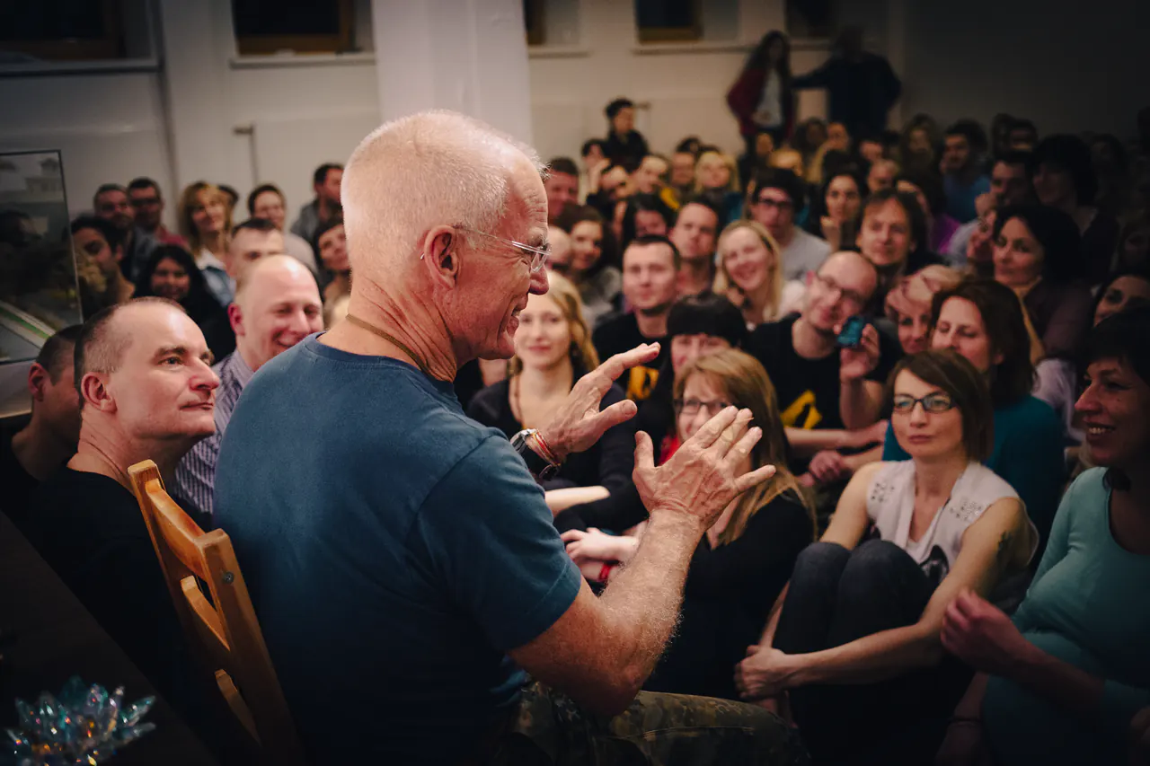 Lama Ole Nydahl speaks with his hands together in front of a crowded room