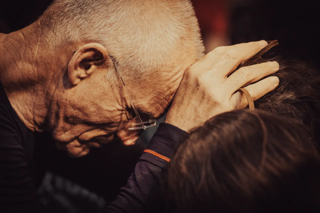 Close-up of Lama Ole Nydahl bowing his head to a person's head, his hand cupping it