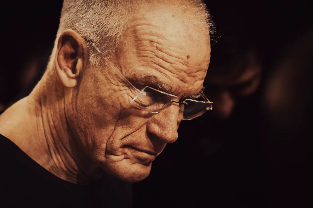 Close-up portrait of Lama Ole Nydahl in glasses, looking down in warm light