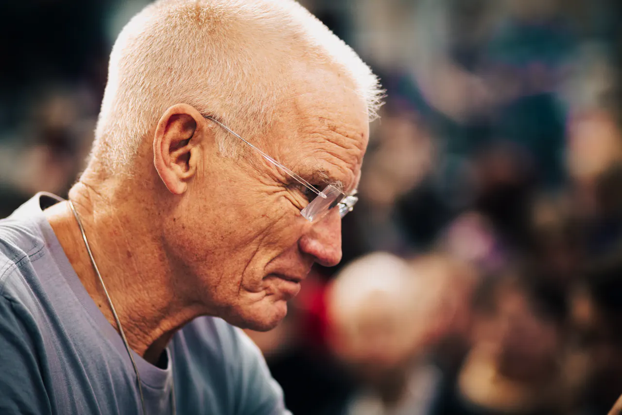 Profile of Lama Ole Nydahl in a grey t-shirt, a blurred crowd behind him