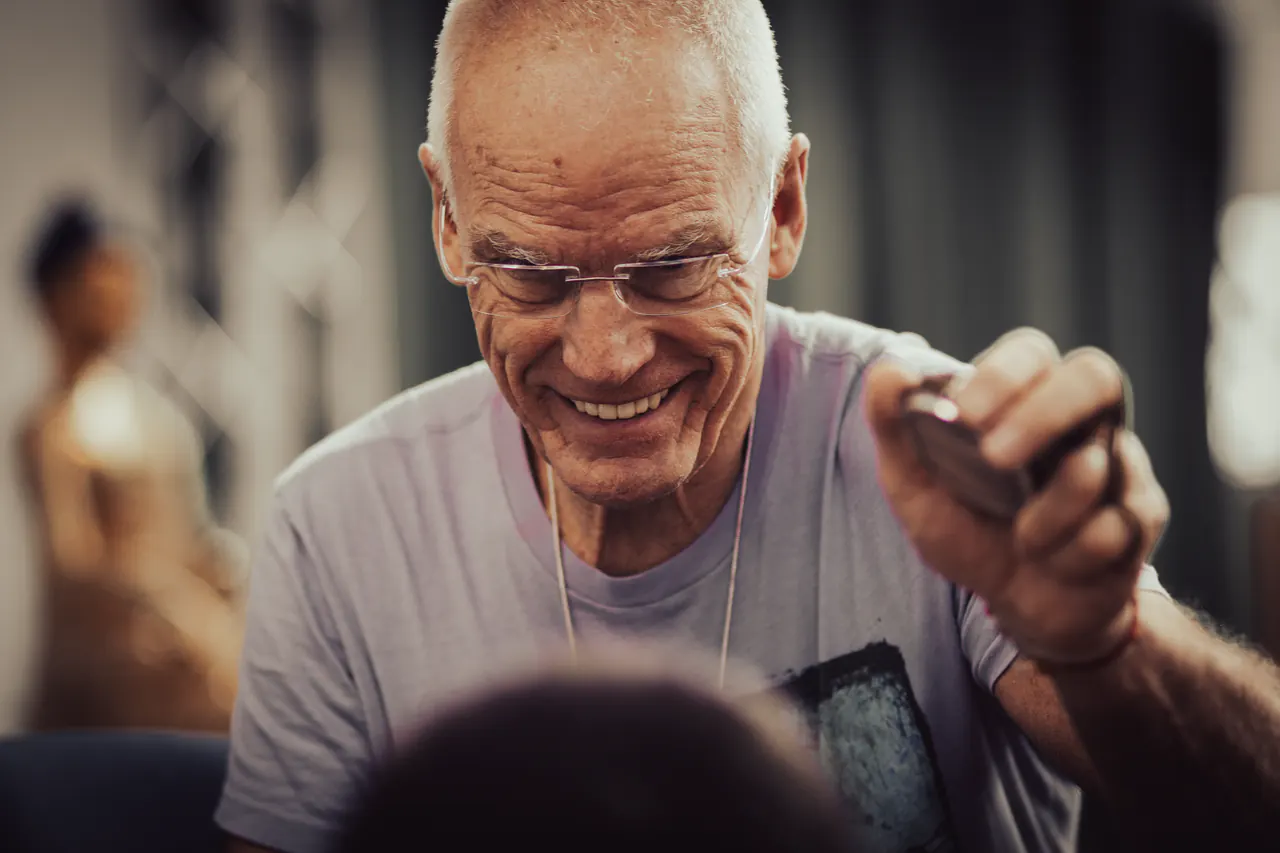 Lama Ole Nydahl smiles broadly as he holds out a small object to someone