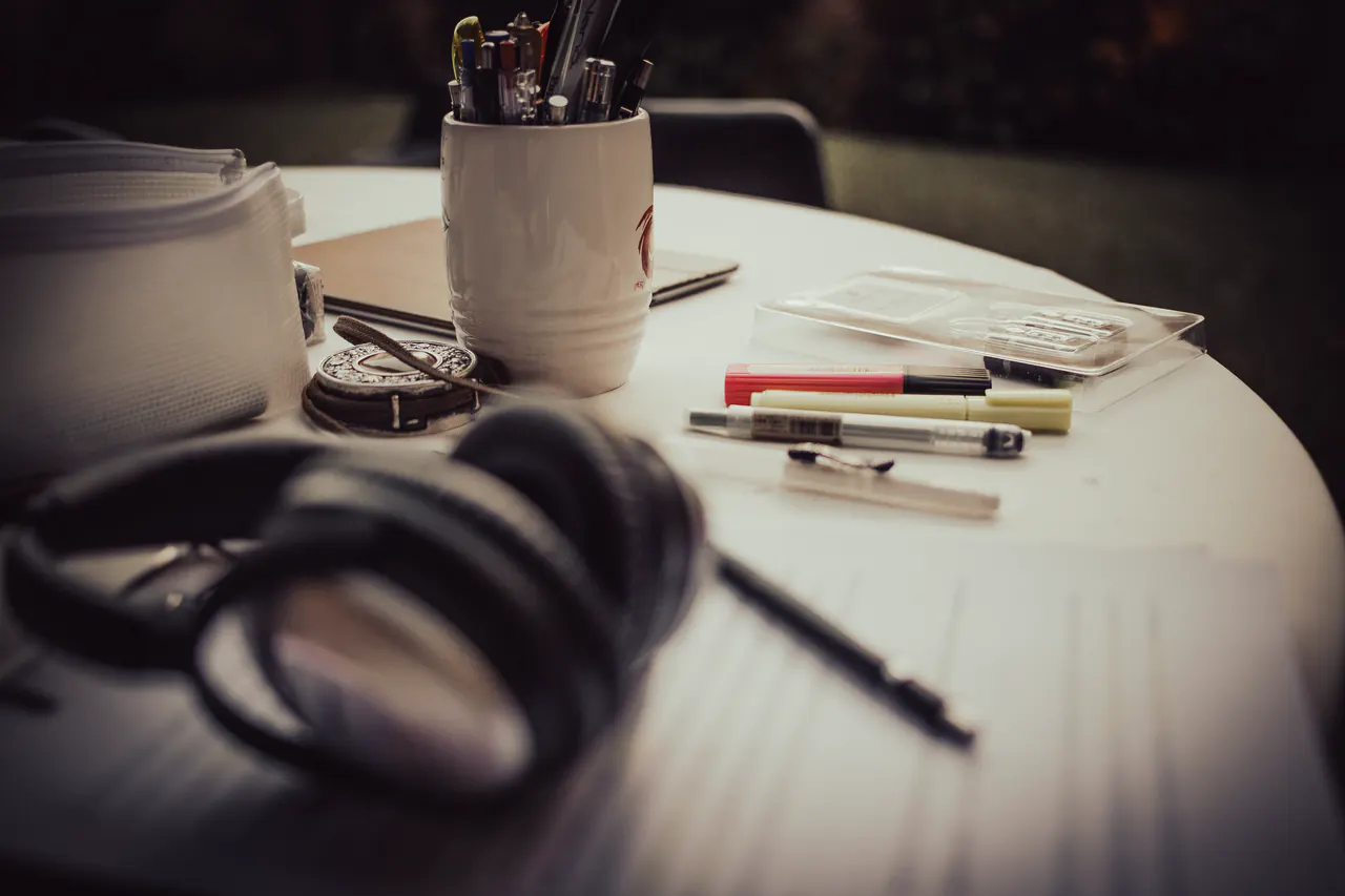 A round table in dim light with headphones, pens in a mug and sheets of paper