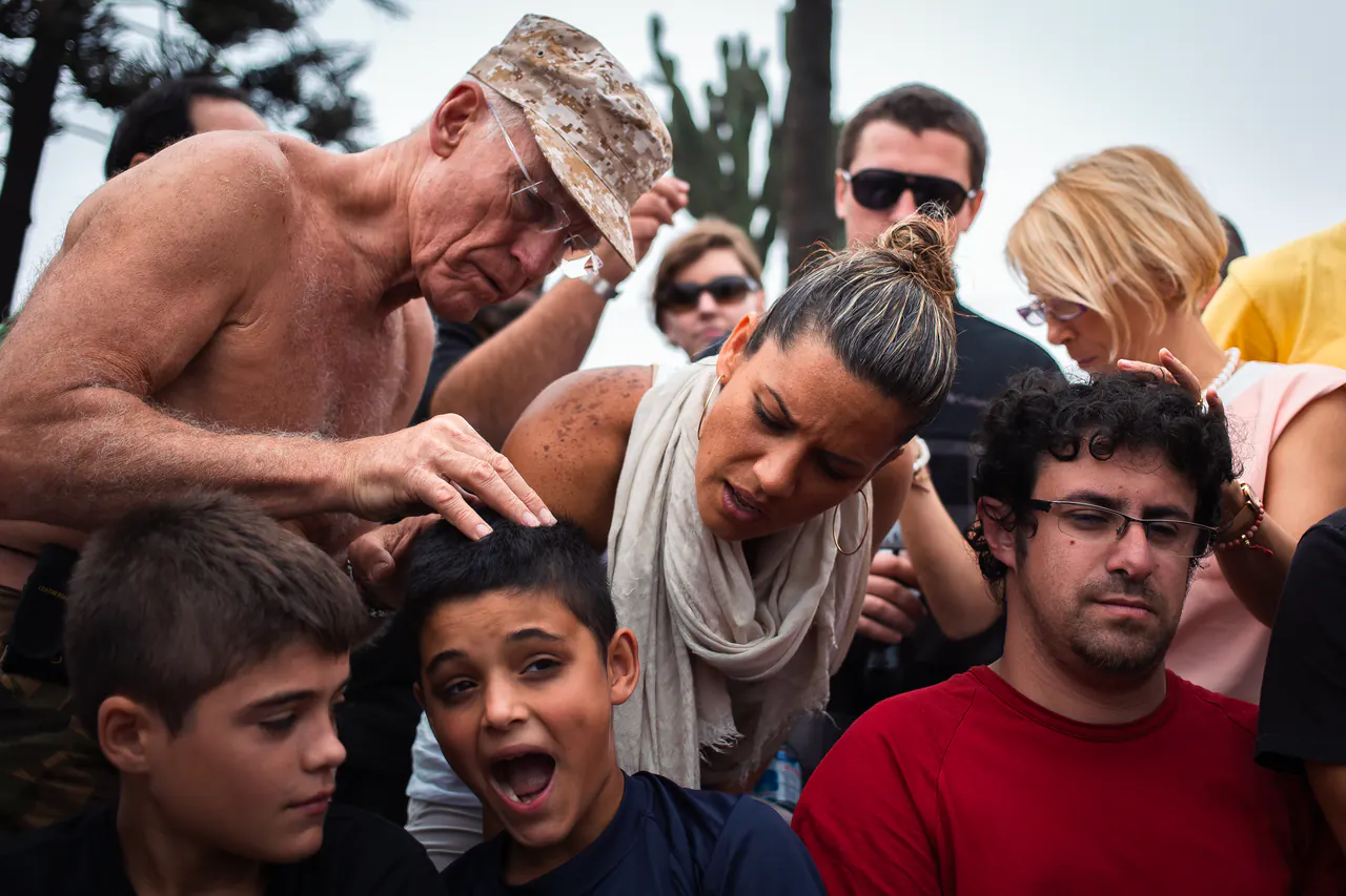 Lama Ole Nydahl in a camouflage cap places his hand on a boy's head among onlookers