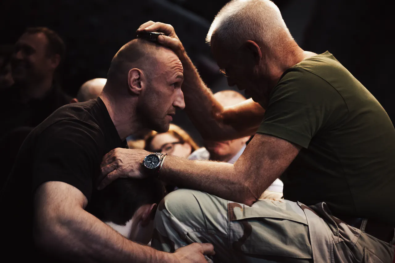 Lama Ole Nydahl presses his hand to the head of a kneeling man in a dark, crowded room
