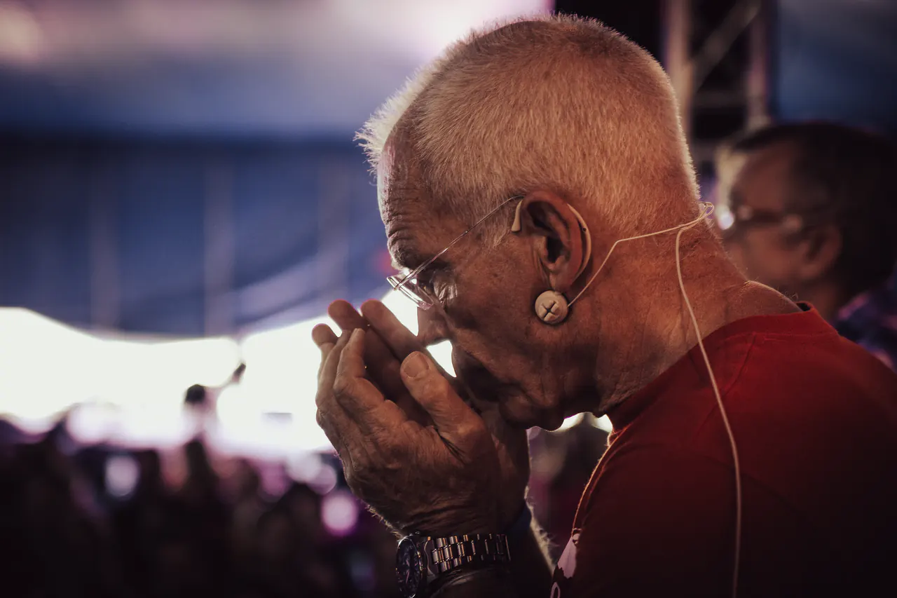 Profile of Lama Ole Nydahl with a headset microphone, his hand raised to his face, inside a tent