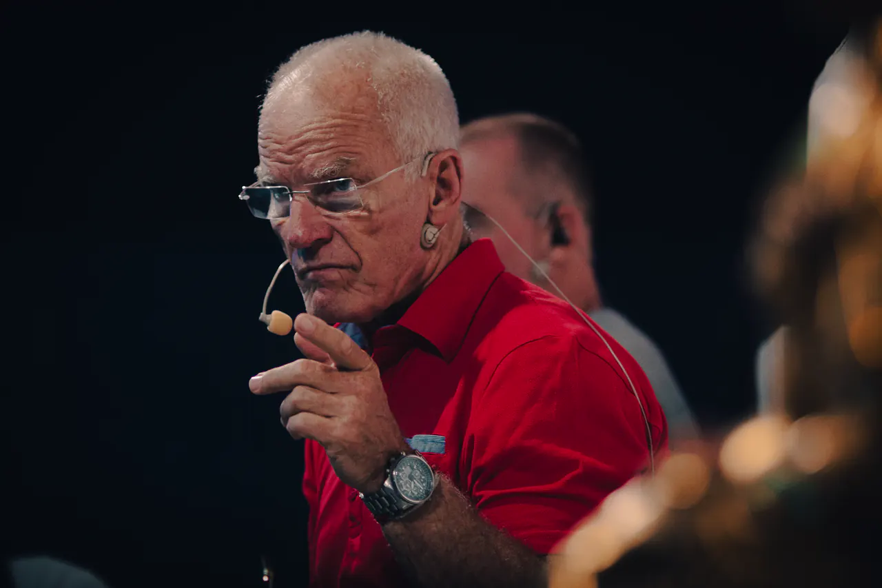 Lama Ole Nydahl listens with a hand at his chin, a golden statue blurred in front of him