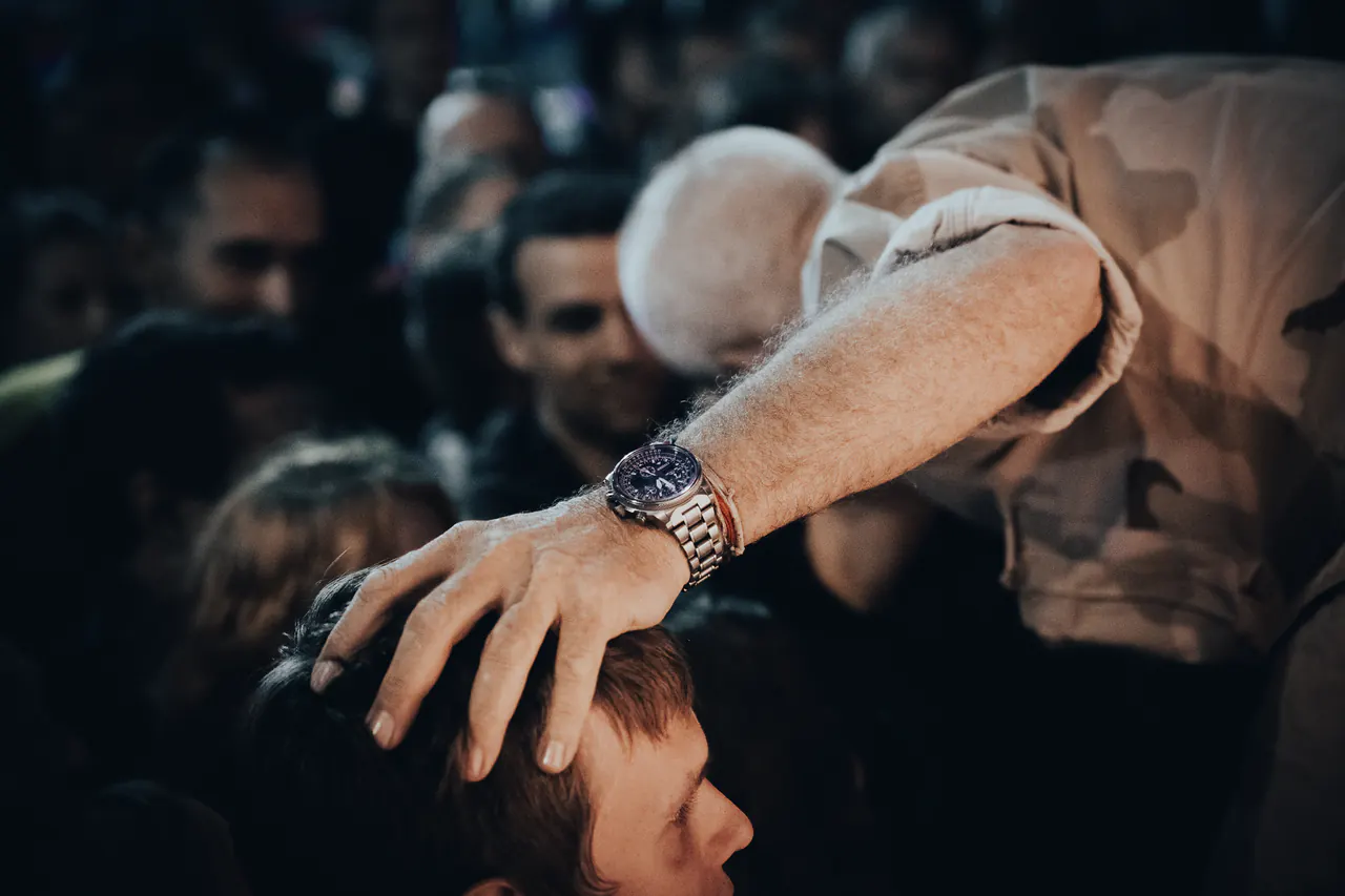 Seen from above, Lama Ole Nydahl lays his hand on a young man's head in a crowd