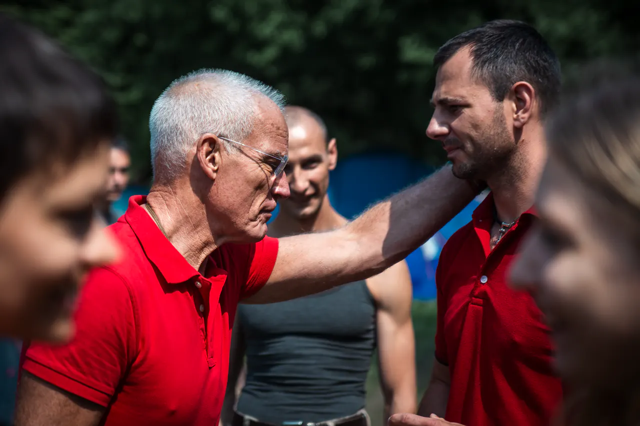 Lama Ole Nydahl rests his hand on a younger man's shoulder among people outdoors